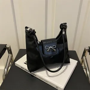 Sac à bandoulière noir élégant avec nœud argenté et lanières nouées sur un livre blanc
