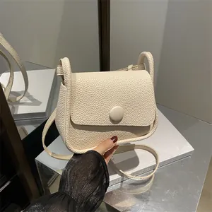 Chic cream leather crossbody bag with lychee texture and round buckle on a mirrored surface