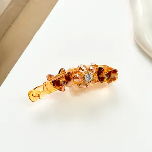 Gros plan d'une pince à cheveux banane en résine ambrée avec perles et cristaux