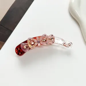 Détail d'une pince banane dégradée avec fleurs roses et strass brillants pour une coiffure élégante