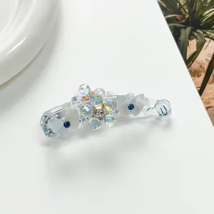 Détail d'une pince à cheveux banane en résine avec papillons blancs et strass bleus brillants