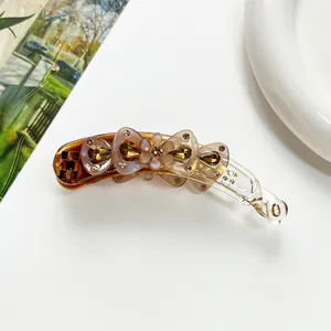 Détail de la pince banane ambre avec fleur crème et strass sur un fond blanc épuré