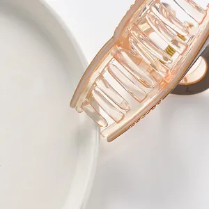 Macro detail of a translucent peach pink acrylic hair claw clip on a white plate