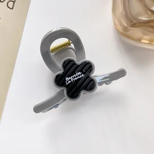 Détail d'une pince à cheveux fleur avec logo blanc sur une table blanche épurée