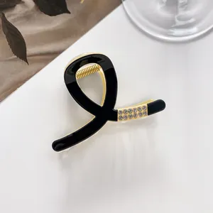 Detail of a small black acrylic hair claw clip with gold metal frame and sparkling rhinestones