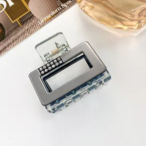 Close-up of square rhinestone hair claw with blue acrylic base and grey metallic finish