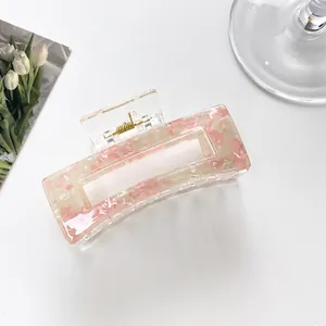 Macro detail of pink marble acrylic hair claw clip with golden spring on white surface