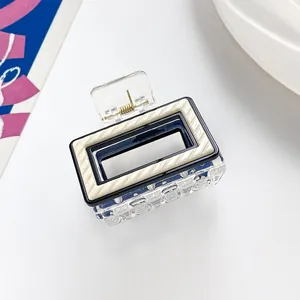 Detail of a rectangular hair claw clip with cream textured stripes and black inner frame