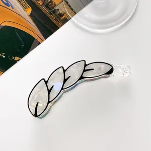 Detail of banana hair clip with white pearlescent leaf design and black outlines