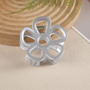 Détail d'une pince à cheveux fleur évidée argent mat sur un plateau en bois épuré