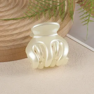 Detail of a pearl white pumpkin-shaped hair claw clip on a natural wooden tray with green leaves