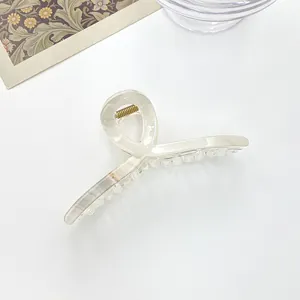 Detail view of a creamy marble pattern hair claw clip with golden metal spring and acrylic finish