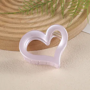 Détail d'une pince à cheveux rose mat en forme de cœur avec design évidé et ressort