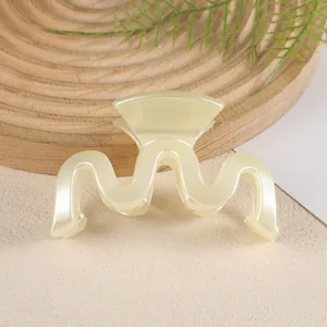 Détail d'une pince à cheveux ondulée crème sur un plateau en bois avec une feuille
