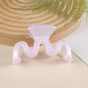 Détail macro d'une pince à cheveux rose ondulée avec finition nacrée sur plateau bois