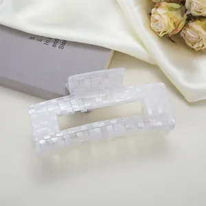 Détail de la pince à cheveux à damier nacré sur un fond élégant en soie et satin