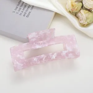 Dettaglio macro della pinza per capelli in acetato rosa marmorizzato su sfondo neutro