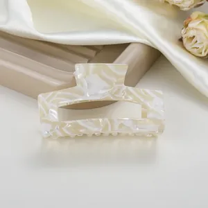 Detalle de pinza de pelo rectangular en acetato crema sobre fondo de seda suave