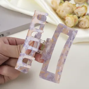 Handheld view of a large rectangular marble purple acetate hair claw clip with gold spring