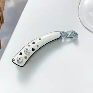 Detailed shot of ivory acetate banana hair clip with rhinestones and clover patterns
