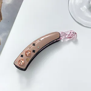Detail of banana clip with pink rhinestones and black clover on beige acetate