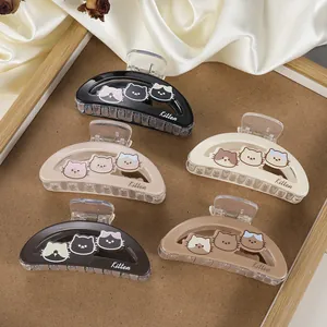 Detail view of five large acrylic cat-themed hair claws in neutral colors on a wooden tray