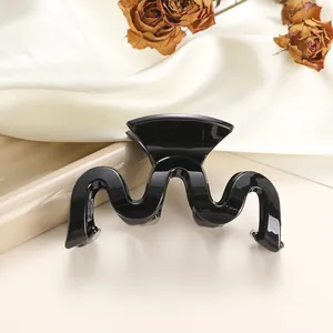 Macro detail of glossy black wavy hair claw clip resting on white silk and ceramic plate