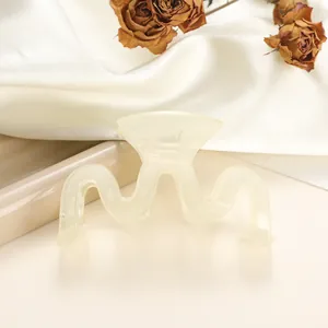 Macro view of a wavy cream-white hair claw clip on elegant silk background fabric