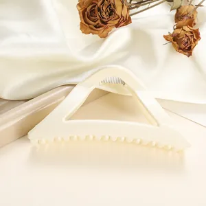 Macro detail of a large ivory triangle claw clip with silver spring on silk background