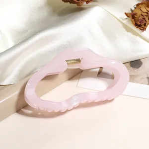 Détail d'une pince à cheveux ondulée rose clair avec finition scintillante et ressort doré