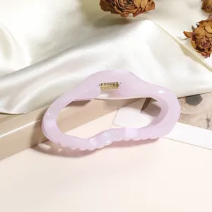 Détail d'une pince à cheveux ondulée lavande avec ressort doré sur du tissu