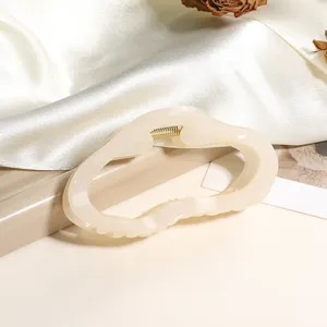 Gros plan d'une pince à cheveux ondulée crème avec ressort en métal doré