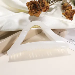 Close-up of pearl white triangle hair claw clip with golden spring on satin fabric
