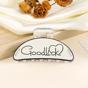 Detail view of cream white 9cm hair claw clip with Good Luck print and rhinestones