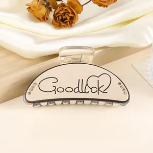 Detail of cream shark hair clip with GoodLuck lettering and shimmering rhinestones