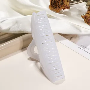 Detail view of a large glossy cream hair claw clip on white silk with dried roses