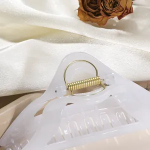 Macro detail of creamy white resin hair claw clip with glitter finish and gold spring