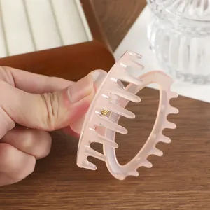 Petite pince à cheveux crabe rose translucide avec ressort doré sur fond en bois