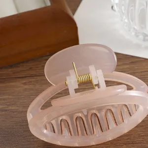 Pince à cheveux rose pâle translucide avec ressort doré sur fond en bois