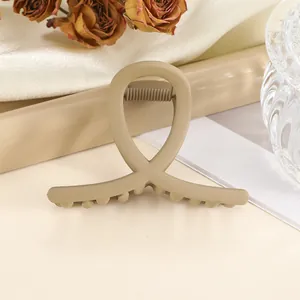 Close-up of a matte beige cross-shaped hair claw clip on elegant silk fabric background