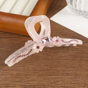 Detailed close-up of a pink resin flower hair claw clip with rhinestones on a wood desk