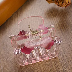 Elegant transparent pink hair claw clip with crystal flowers on a wooden desk surface