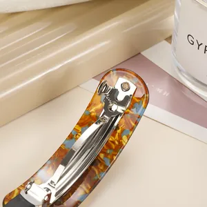 Elegant tortoiseshell acetate spring hair clip with amber and blue flecks shown on a desk