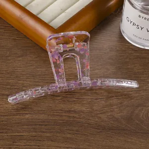 Grande pince à cheveux transparente avec taches colorées sur une surface en bois