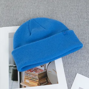 Detail of blue wool knit beanie with ribbed texture and small logo label on grey background
