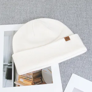 Detail shot of ivory wool knit beanie featuring a brown leather mountain logo patch