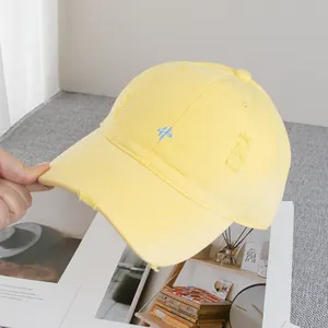 Detailed view of yellow cotton baseball cap with blue embroidery and distressed edges