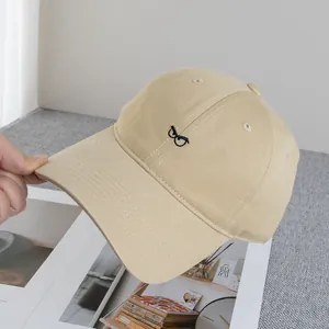 Dettaglio del berretto da baseball in cotone beige con ricamo a occhiali e cuciture sulla visiera