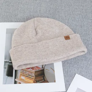 Detailed texture of beige wool knit beanie featuring a brown leather mountain logo patch