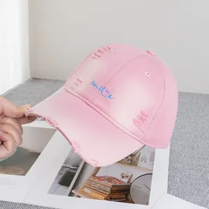 Detail of pink distressed cotton baseball cap with blue smile embroidery and frayed brim
